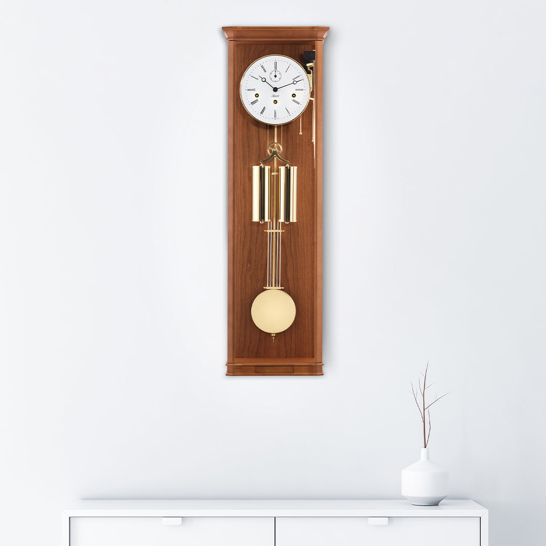 Light Cherry wood regulator wall clock with brass highlights hanging on white wall above white dresser
