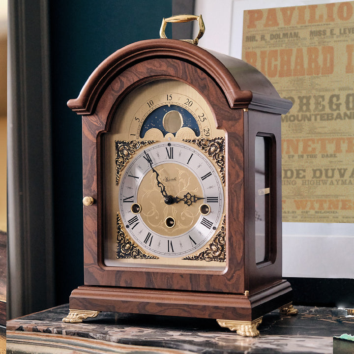 Front, side view of vintage style luxury walnut mantel clock with traditional clock face, featuring moon phase dial.